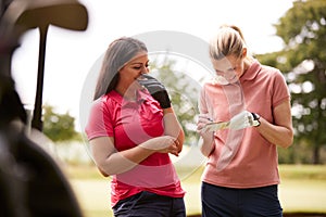 Two Women Playing Golf Marking Scorecard With  Buggy In Foreground