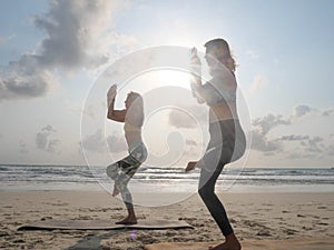 Two women practice eagle yoga asana at sea beach in sunshine