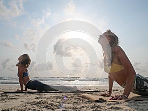 Two women practice upward facing dog yoga pose at seaside at sunset