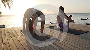 Two women practice yoga in seaside hotel lounge zone at sunset