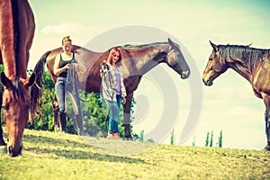 Two women relaxing with horses on meadow