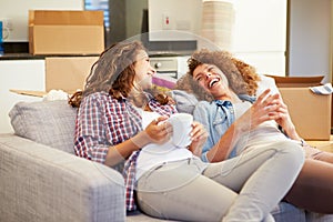 Two Women Relaxing On Sofa With Hot Drink In New Home