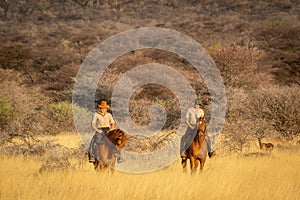Two women riding horses watched by impala