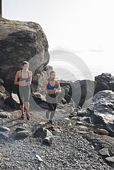 Two women running on the beach near rocks