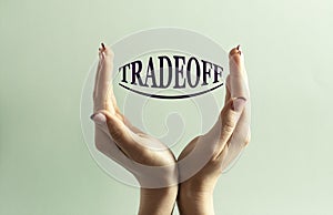 Two women`s hands hold the word TRADEOFF against a mint background