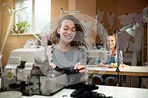 Two women seamstresses work in the workshop on sewing machines smile