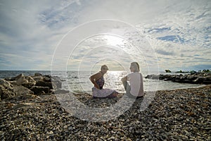 Two women sit on a pebble beach and relax as the sunset