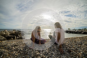 Two women sit on a pebble beach and relax as the sunset