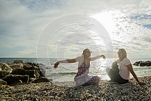 Two women sit on a pebble beach and relax as the sunset