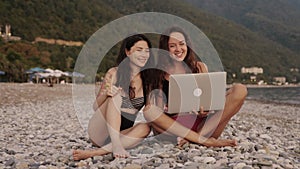 Two women sitting on the beach and talking on video conference with friends. Social distancing during pandemic. People
