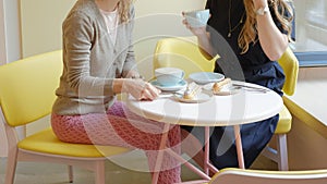 Two women sitting in a cafe restaurant eating cakes eclair drinking coffee and laughing