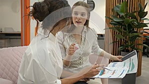 Two women sitting on the couch in the office talking and discussing work schedules, office workers, office, documents