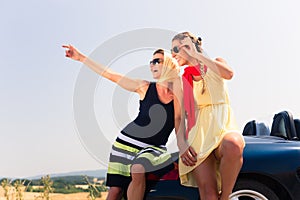 Two women sitting on hood of convertible car