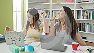 Two women sitting on table singing song studying at library university