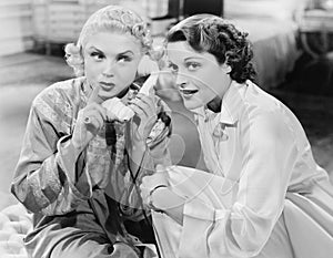 Two women sitting together and listening on the telephone receiver