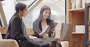 Two women sitting and working in a modern and industrial style cafe. Two multiethnic colleagues working on laptop and