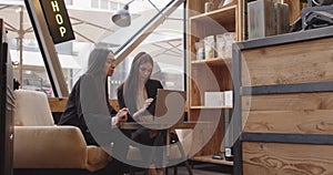 Two women sitting and working in a modern and industrial style cafe. Two multiethnic colleagues working on laptop and