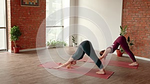 Two women in sports uniform makes smooth body wave in yoga studio. Healthy lifestyle concept.