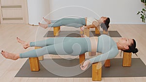 Two women in sportswear lies on the yoga blocks in the savasana pose in studio