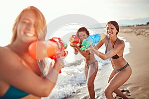 Two women spurt a female friend with water guns on a sandy beach