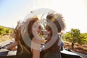 Two women standing in the back of open car turning to camera