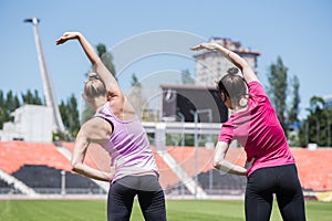 Two women are stretching. Workout at the stadium.