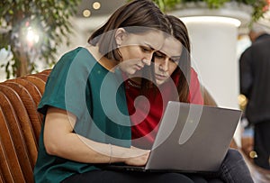 Two women students studying in open space with laptop computer.