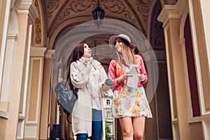 Two women tourists talking while going sightseeing in Odessa. Happy friends travelers using map and drinking coffee