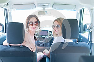 Two women turn around while sitting in the front seats of the car. Girlfriends travel by car