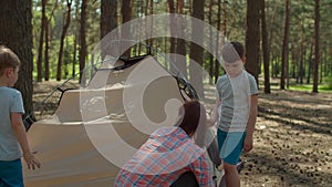 Two women and two boys having summer camping vacation in forest. Happy family of two mothers and two sons put up tent