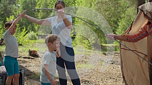 Two women and two boys having summer camping vacation in forest. Happy family of two mothers and two sons put up tent