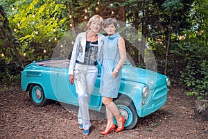 Two women in a vintage car. happy senior mother and adult daughter stand by a retro convertible