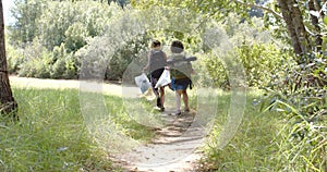 Two women walk along a narrow trail in a lush, green forest setting, collecting trash