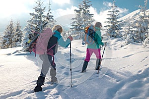 Two women walk with snowshoes on the backpacks in winter trekking