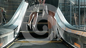 Two women walking along shop windows with shopping bags in hands go to escalator, modern office