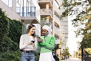 two women walking down a street looking phones