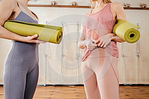 Two women wearing activewear holding yoga mats standing in sport studio