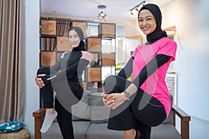 two women wearing a headscarf smiling while doing lunges movements while exercising indoors