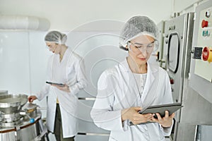 Two women wearing lab coats working at factory in food or pharma production