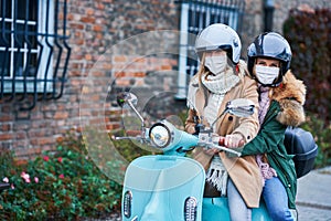 Two women wearing masks and commuting on scooter