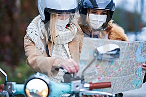 Two women wearing masks and commuting on scooter holding map