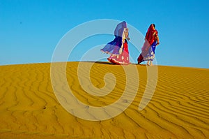 Two women wearing traditional ethnic indian outfits walking on a yellow sand dune