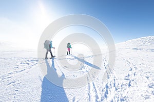 Two women on a winter hike. Girlfriends with trekking sticks go along a snow-covered mountain path. Girls with backpacks and