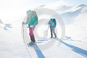 Two women on a winter hike. Girlfriends with trekking sticks go along a snow-covered mountain path. Girls with backpacks and