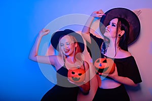 Two women witches hold pumpkins in their hands and dance. Women in neon lights are celebrating a Halloween party. Models smile and