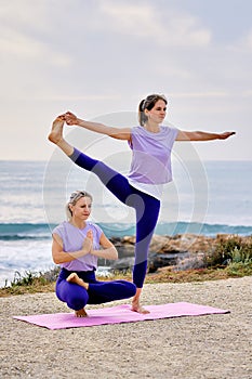 Two women women do yoga exercises near sea
