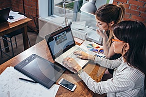Two women working on new website design choosing pictures using the laptop surfing the internet