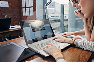 Two women working on new website design choosing pictures using the laptop surfing the internet