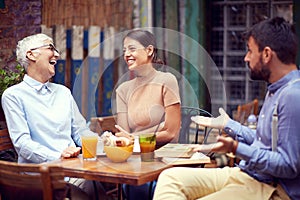 Two women, young adult and elderly, making fun of beardy guy, looking each other, laughing, smiling