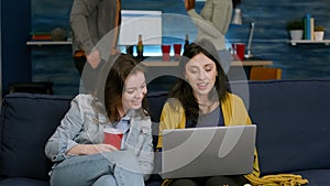 Two womens sitting on couch watching comedy series on laptop computer